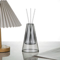 STUDIO NOÉRA Élane clear borosilicate glass diffuser bottle with a tall geometric design and included reed sticks.