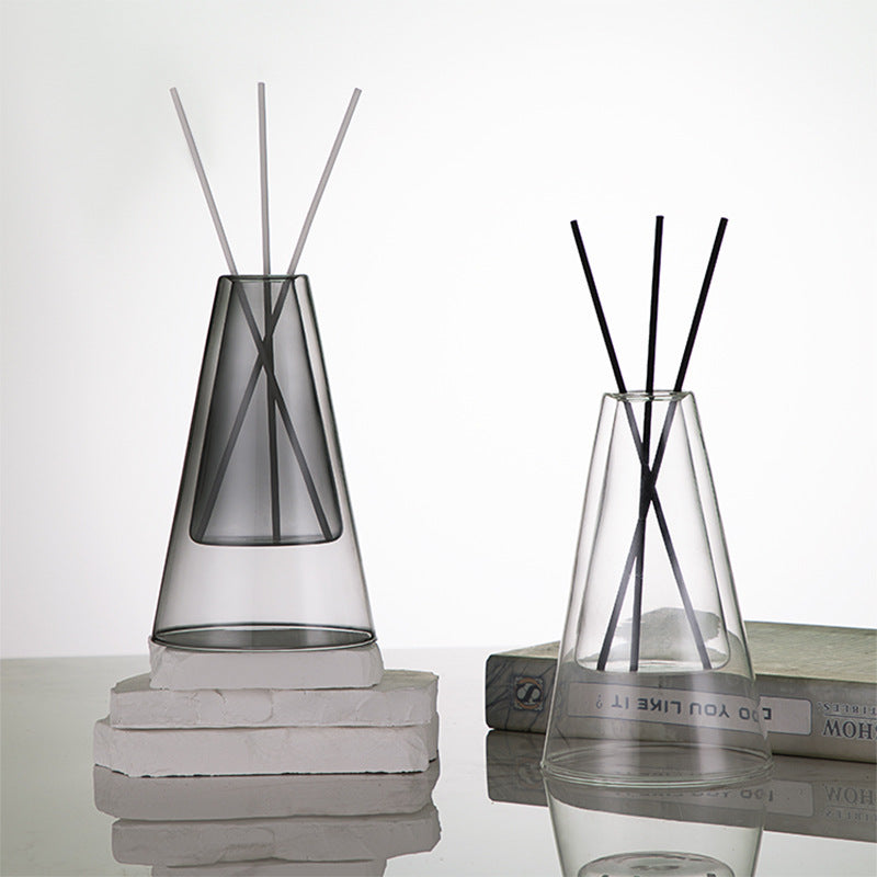 STUDIO NOÉRA Élane clear borosilicate glass diffuser bottle with a tall geometric design and included reed sticks.