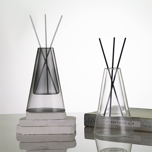 STUDIO NOÉRA Élane clear borosilicate glass diffuser bottle with a tall geometric design and included reed sticks.